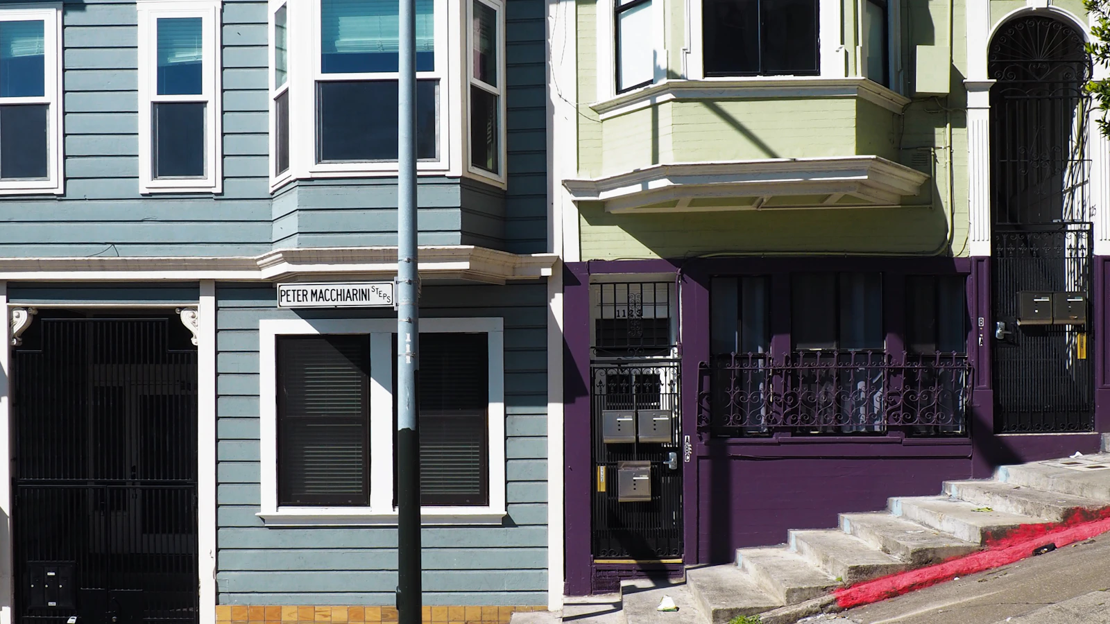 Bay windows and front entrances of homes beside a steep San Francisco sidewalk.